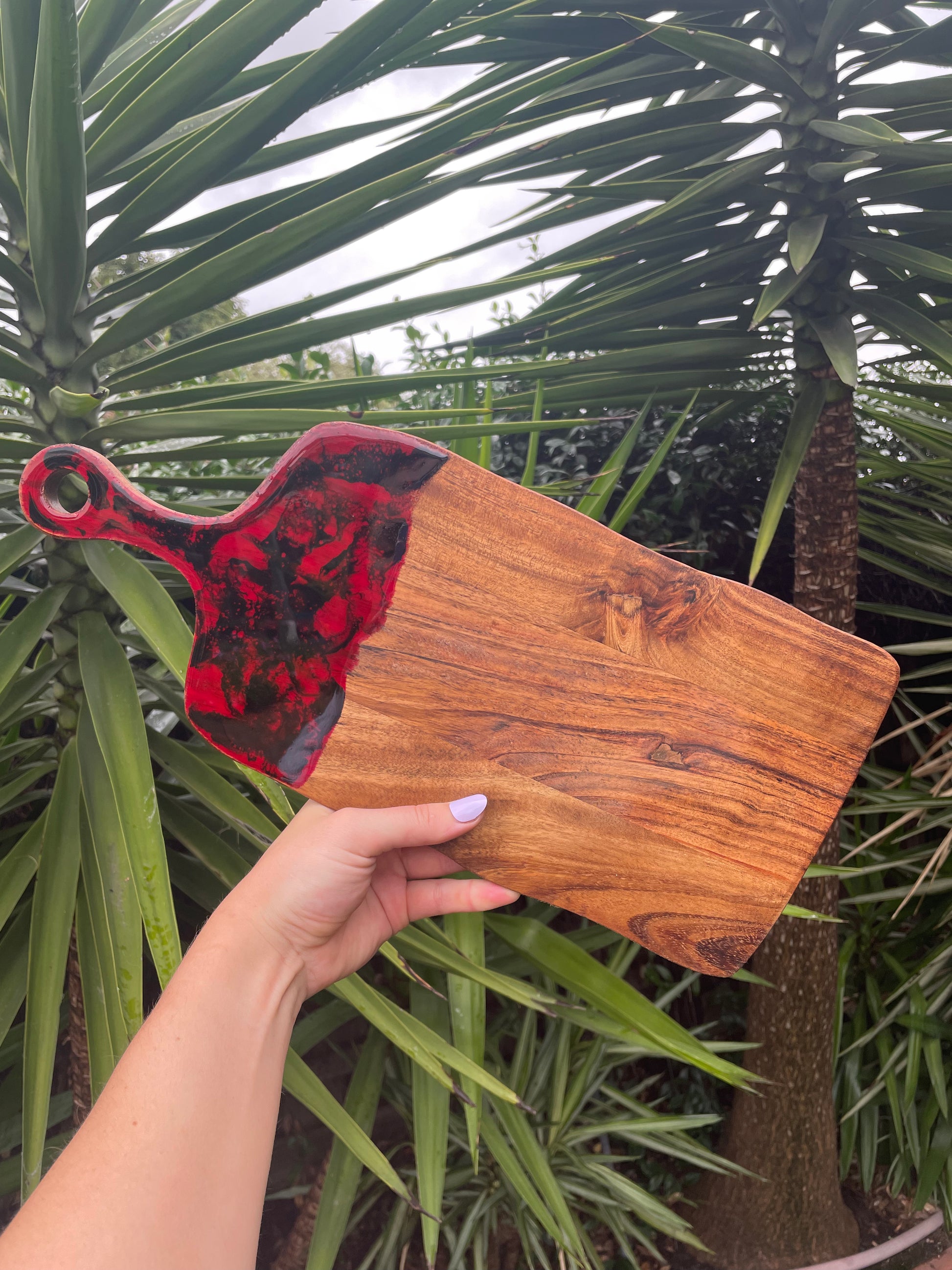 Small acacia wood cheese board with red and black resin swirls covering the handle